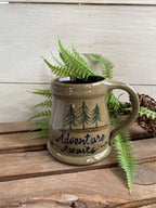 Rowe Pottery Hand thrown stoneware mug In a hand decorated adventure awaits pattern on wooden background with greens