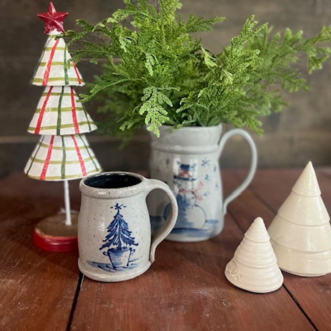 Rowe Pottery handmade Decorative items including a stoneware mug with a potted pine design, a small ceramic tree, and a potted plant on a wooden surface.