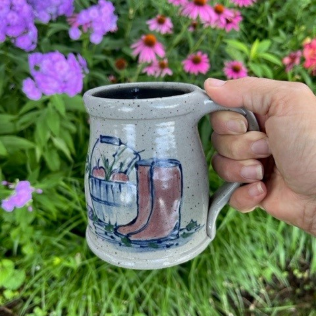 Rowe Pottery Hand thrown stoneware mug In a hand decorated Boots pattern being held up with flower background